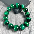 Polished green tiger eye stone bead bracelet on a wrist, showing geometric bead shapes.