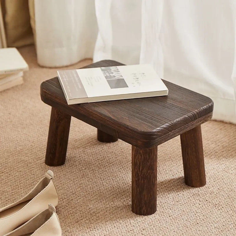 Distressed solid wood shoe changing stool with bracket structure, shown in a hallway setting.