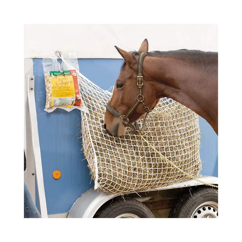 Black woven grid horse feeding bag hanging, filled with hay, for cattle or sheep.
