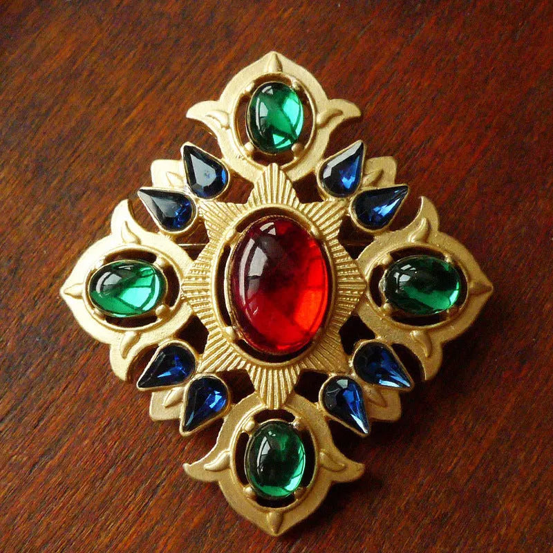 Close-up of a vintage baroque style zinc alloy brooch with a diamond shape on a dark fabric background.