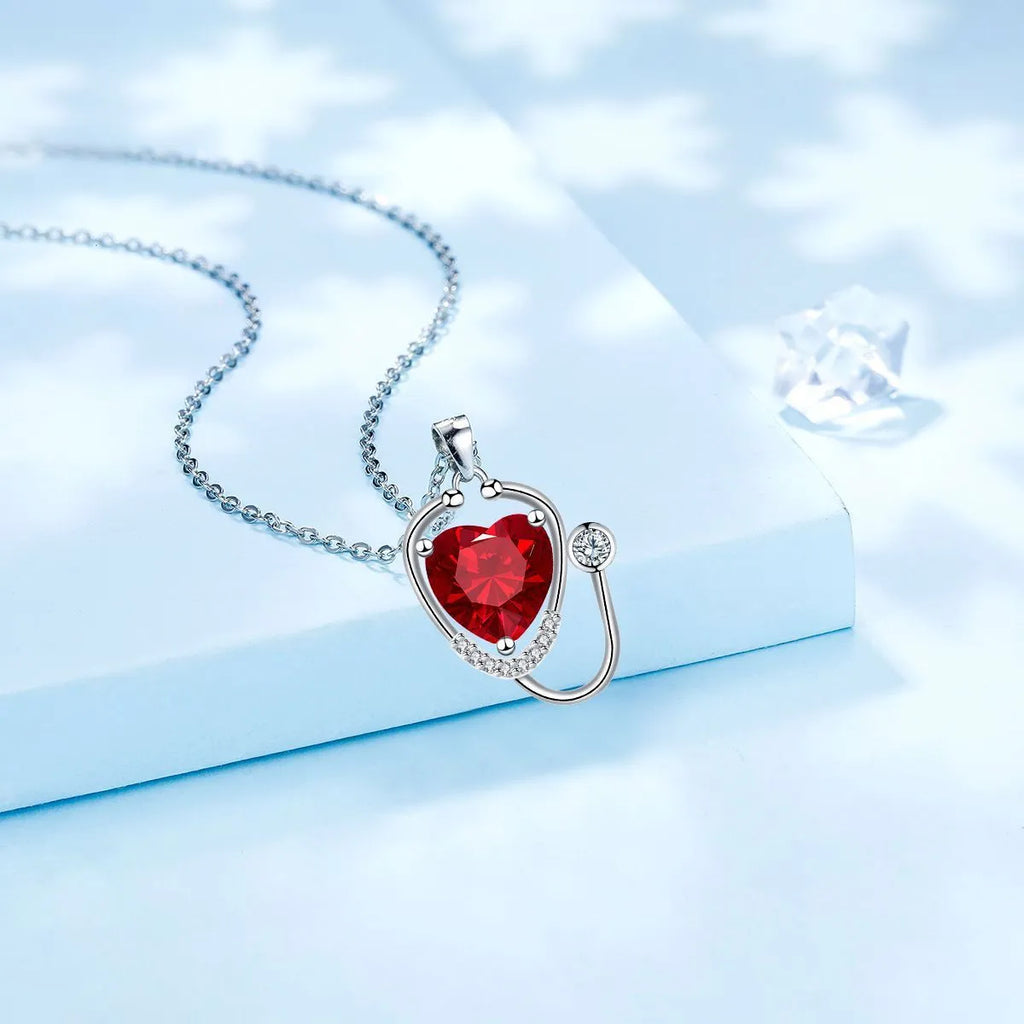 Red diamond coloured women's necklace with wings, cross, and stethoscope pendant.