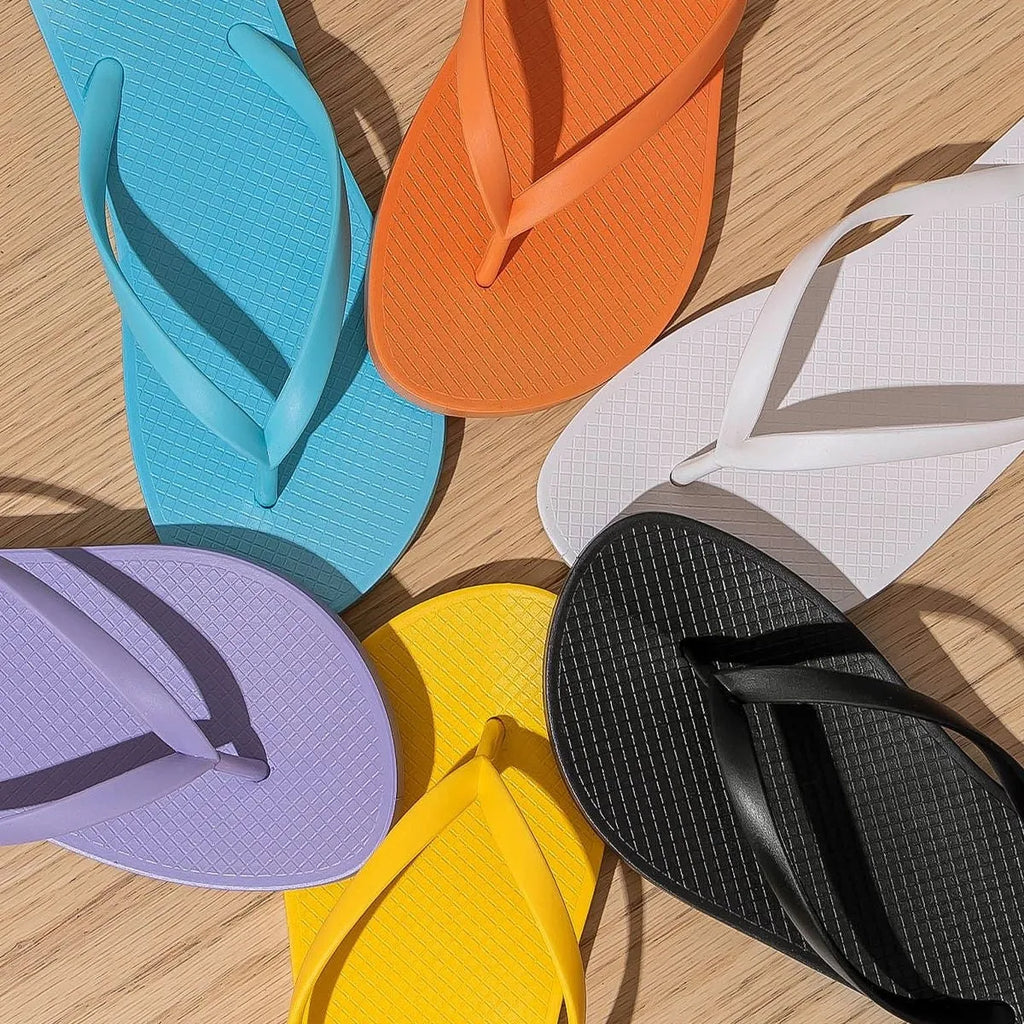 Foldable flat slippers with hollow-out plastic uppers and non-slip PVC soles in orange, purple, black, or white.