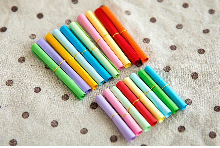 Colourful assortment of miniature rolled paper scrolls with metal eyelets for drift bottle messages.