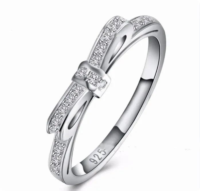 Silver electroplated bow-shaped ring with zircon crystal stones on a finger.