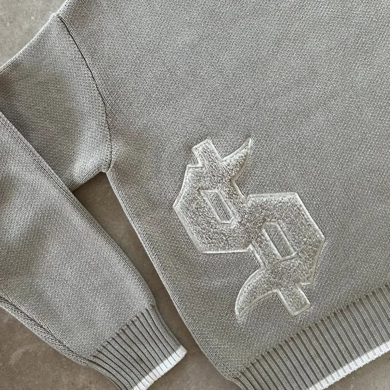 Grey loose-fitting jacquard knit pullover coat with long sleeves on a hanger.