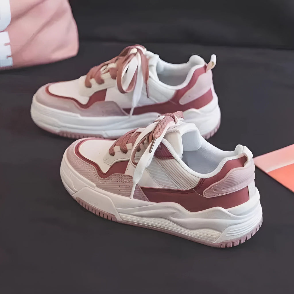 Women's pink and white low top imitation leather sneaker with rubber sole on a neutral background.