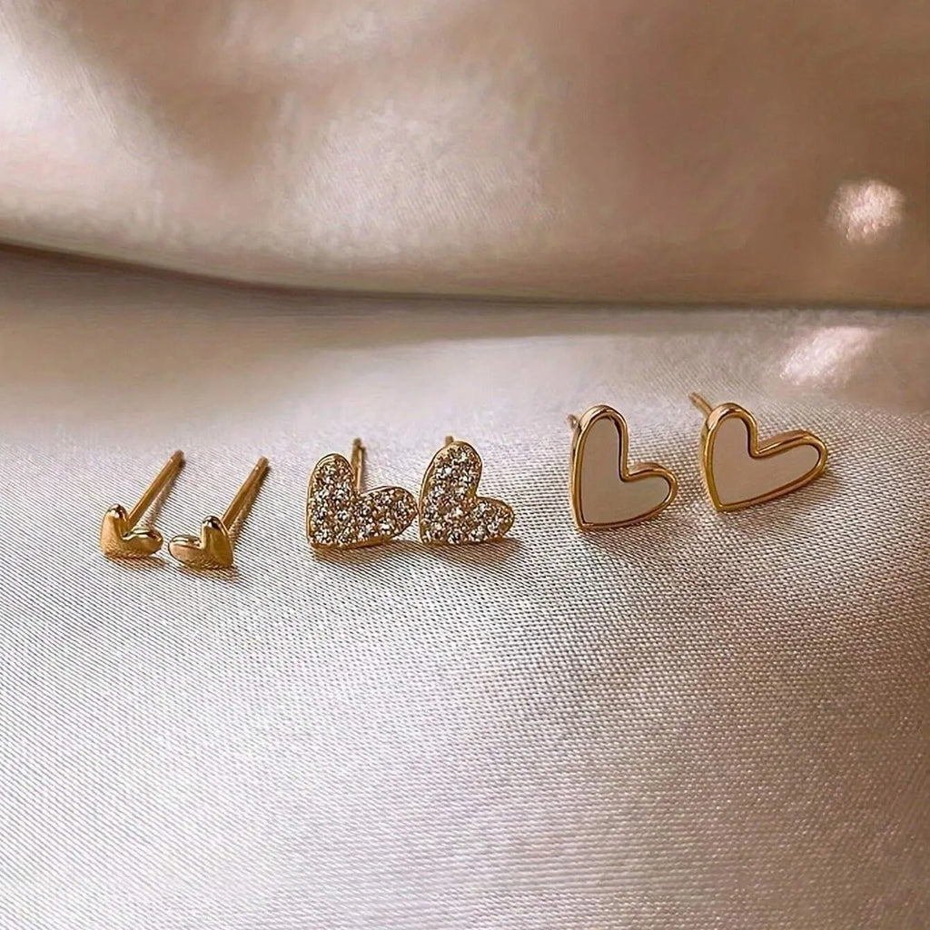 Three pairs of women's heart-shaped alloy earrings in gold, black, and pink colours on a white background.
