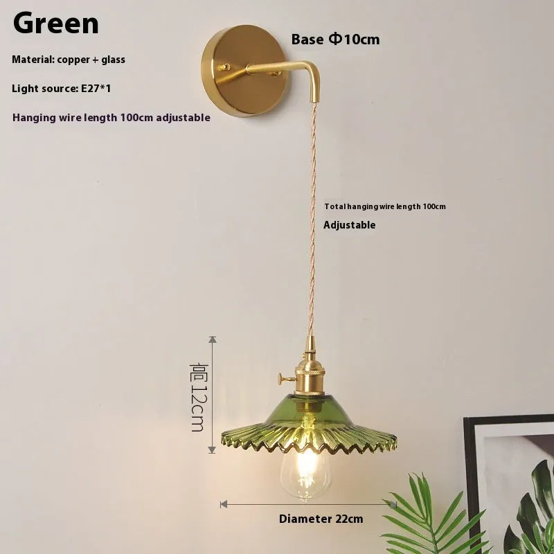 Brass lotus-shaped wall lamp with glass shade in choice of six colours on a plain wall.