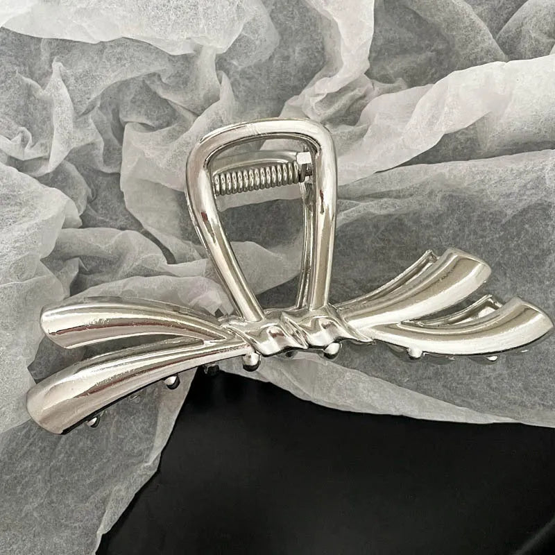 Assortment of silver metal hair claw barrettes with various designs including bows, pearls, and geometric shapes.