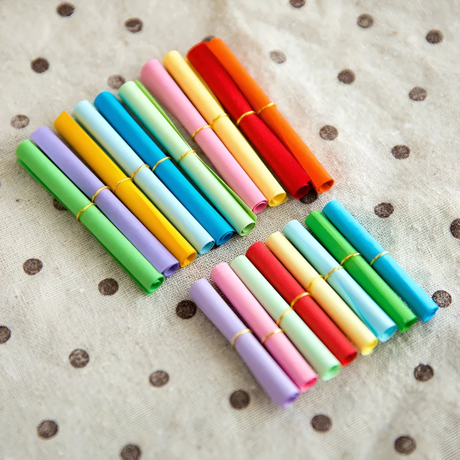 Colourful assortment of miniature rolled paper scrolls with metal eyelets for drift bottle messages.