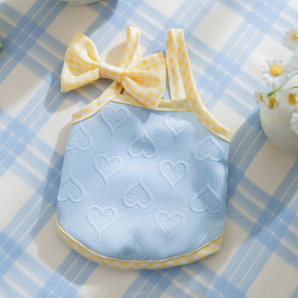 Small dog wearing a blue vest with suspenders and a heart-shaped bow, showing elastic sides.
