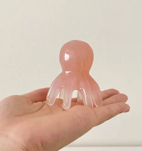 Pink natural resin octopus-shaped massage comb for periocular meridian relief with storage bag.