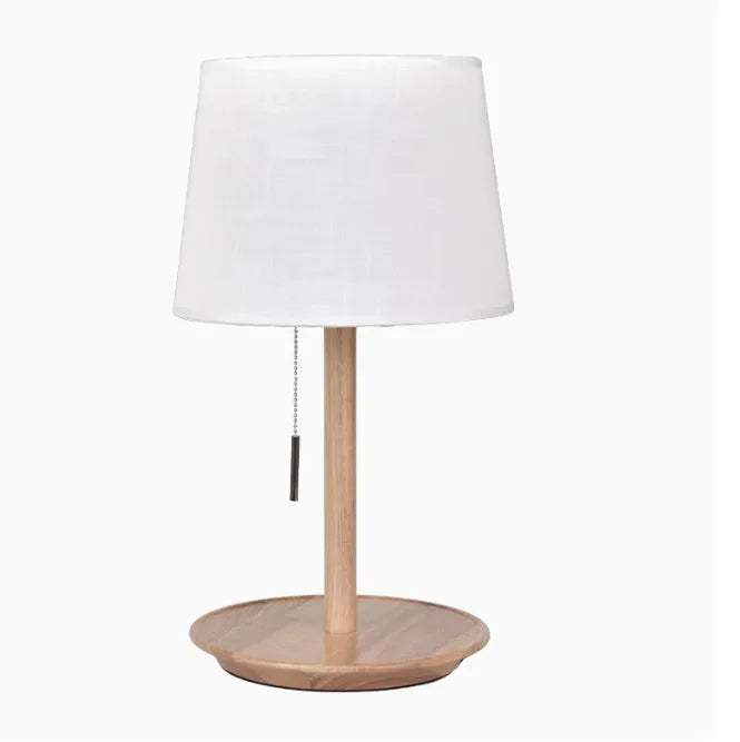 Walnut-colour solid wood desk lamp with a white fabric shade on a wooden table.