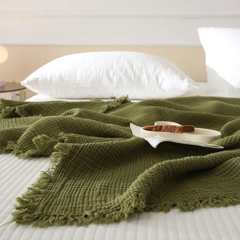 Four-layer gauze cotton blanket with tassel trim in avocado green colour draped over a sofa