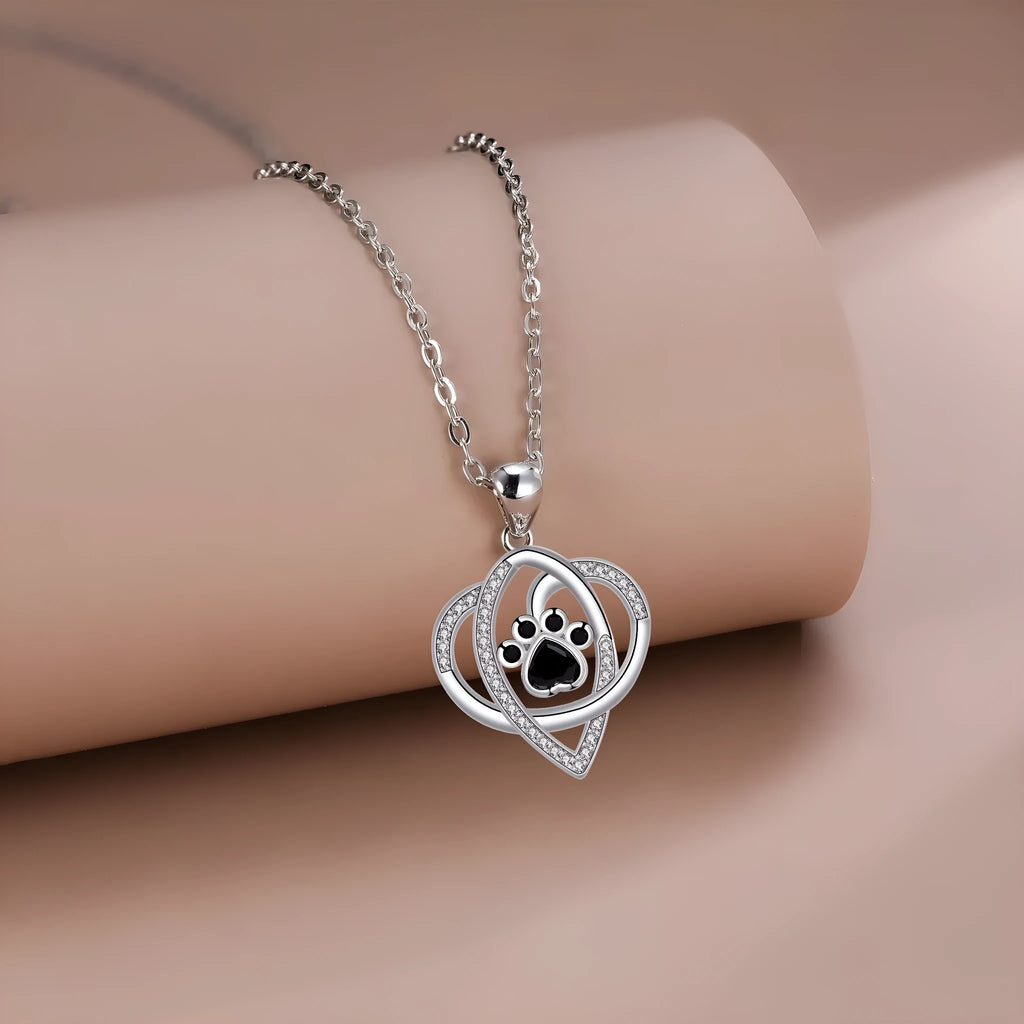 Close-up of a copper necklace pendant showing detailed cat and dog paw prints on a cross chain.