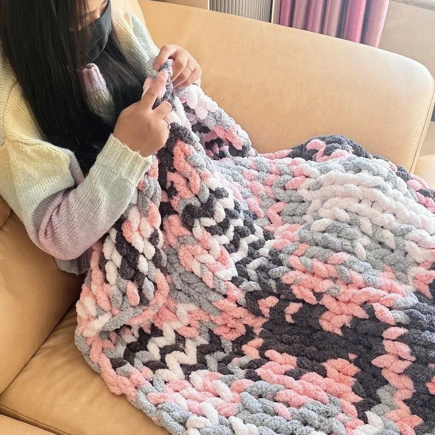 Coarse yarn chenille knitted blanket with braided gravity trim in a modern colour on a bed.