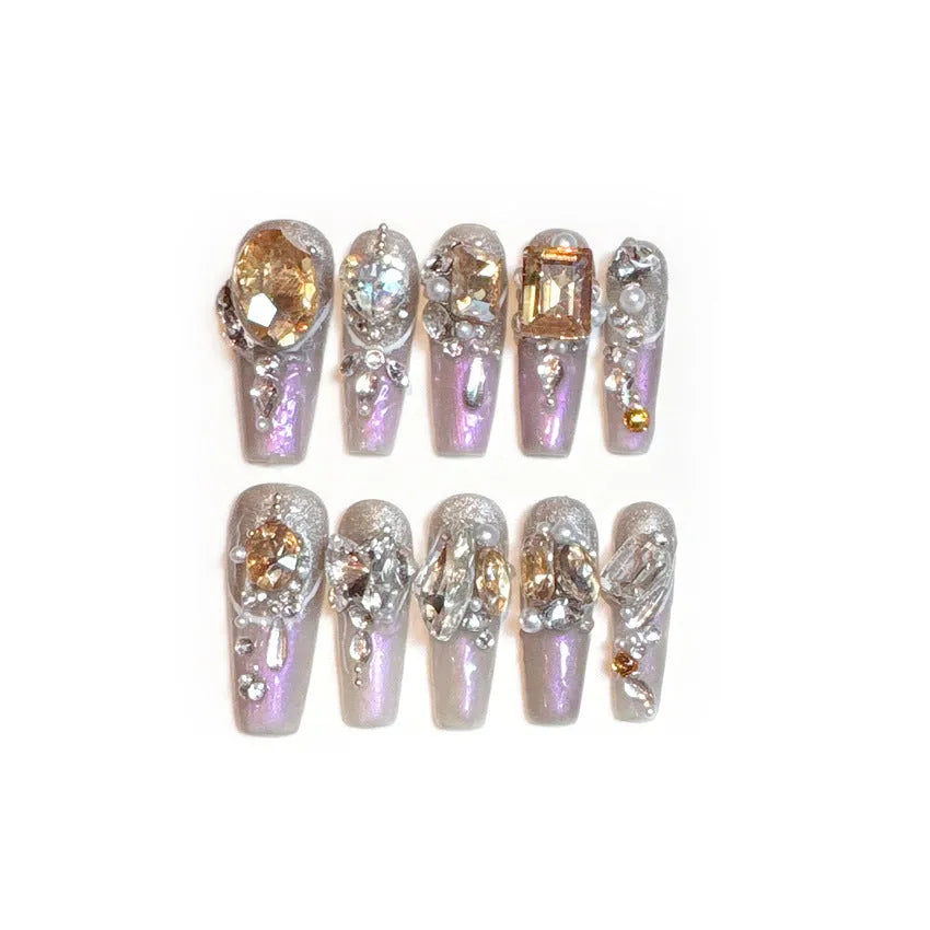 False nail patches with large rhinestones on card, shown with jelly adhesive pot and nail tools.