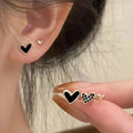 Three pairs of women's heart-shaped alloy earrings in gold, black, and pink colours on a white background.