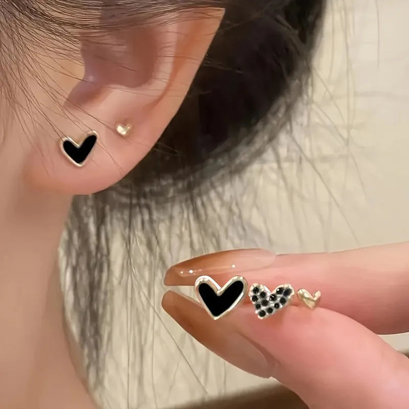 Three pairs of women's heart-shaped alloy earrings in gold, black, and pink colours on a white background.