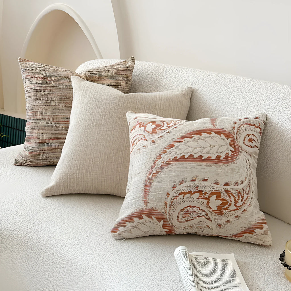 Amber-coloured jacquard pillow cover with paisley and flower pattern, shown in 45x45cm size on a sofa.