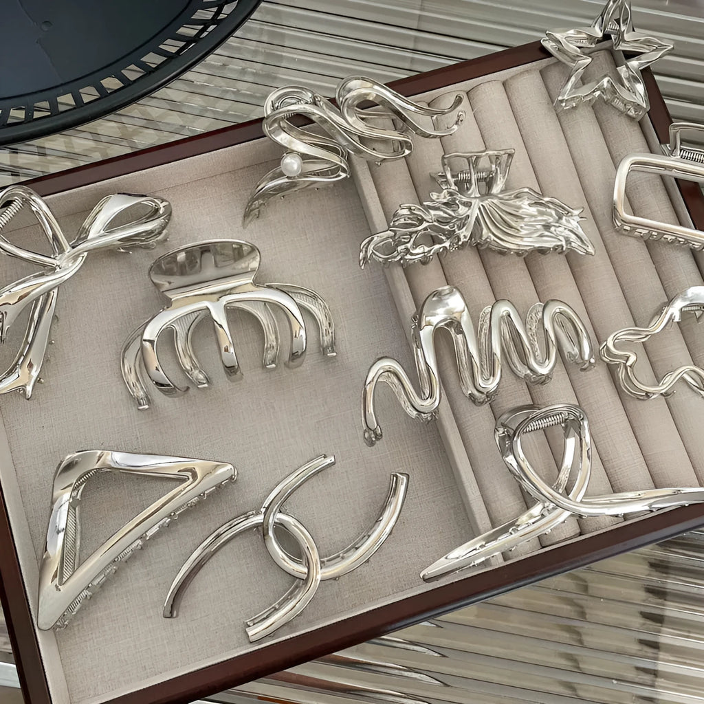 Assortment of silver metal hair claw barrettes with various designs including bows, pearls, and geometric shapes.