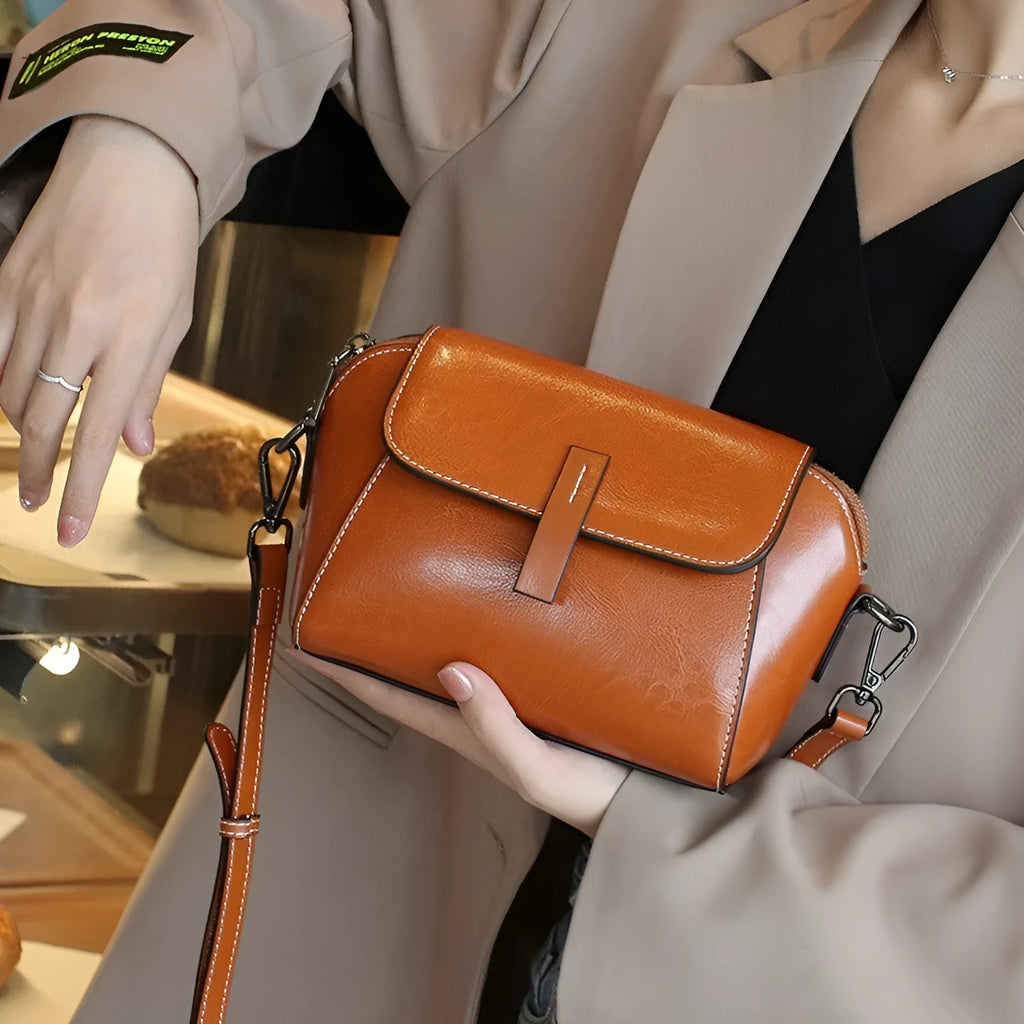 Brown genuine leather women's messenger bag with cross-body strap showing internal zipper compartments