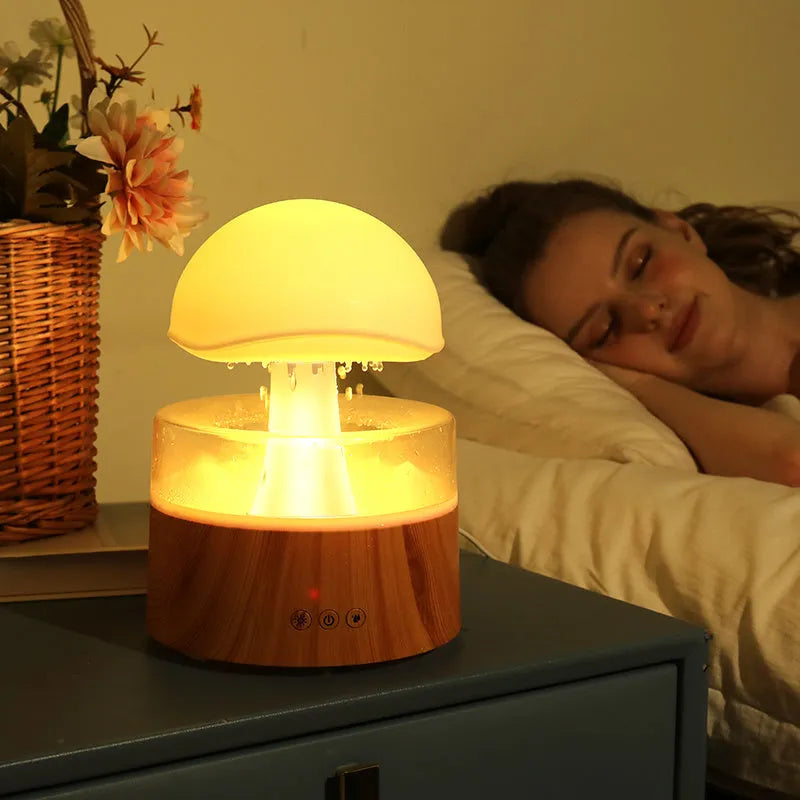 White cloud-shaped humidifier and aroma diffuser with LED lights and mist output on a wooden table.