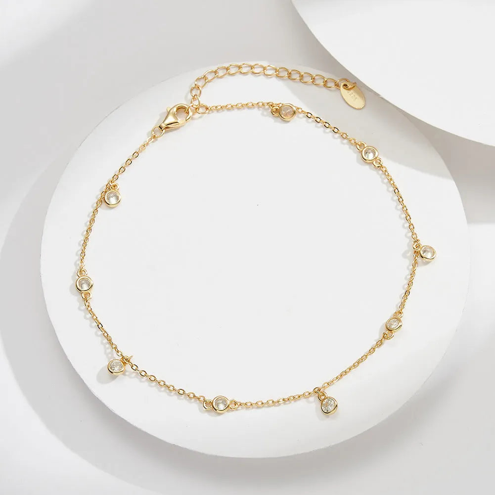 Close-up of a women's silver anklet with a small geometric zirconium pendant on a fine, adjustable chain.