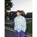 Man wearing a blue loose-fit long sleeve shirt with an embossed three-dimensional floral pattern.