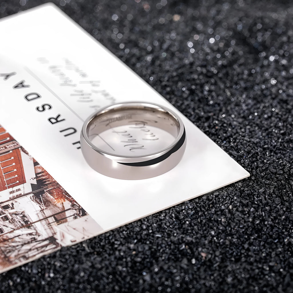Polished silver titanium steel ring on a finger, showing a minimalist band design.