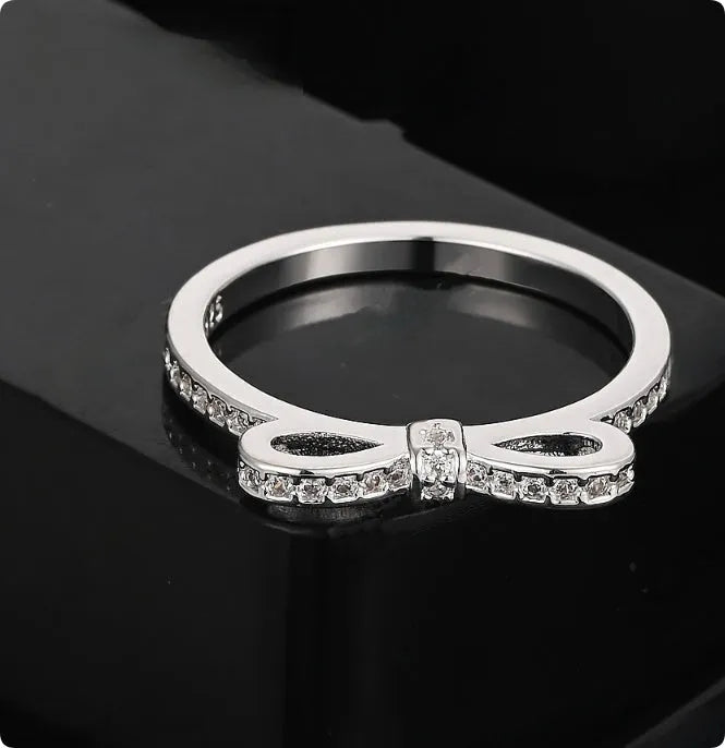 Silver electroplated bow-shaped ring with zircon crystal stones on a finger.