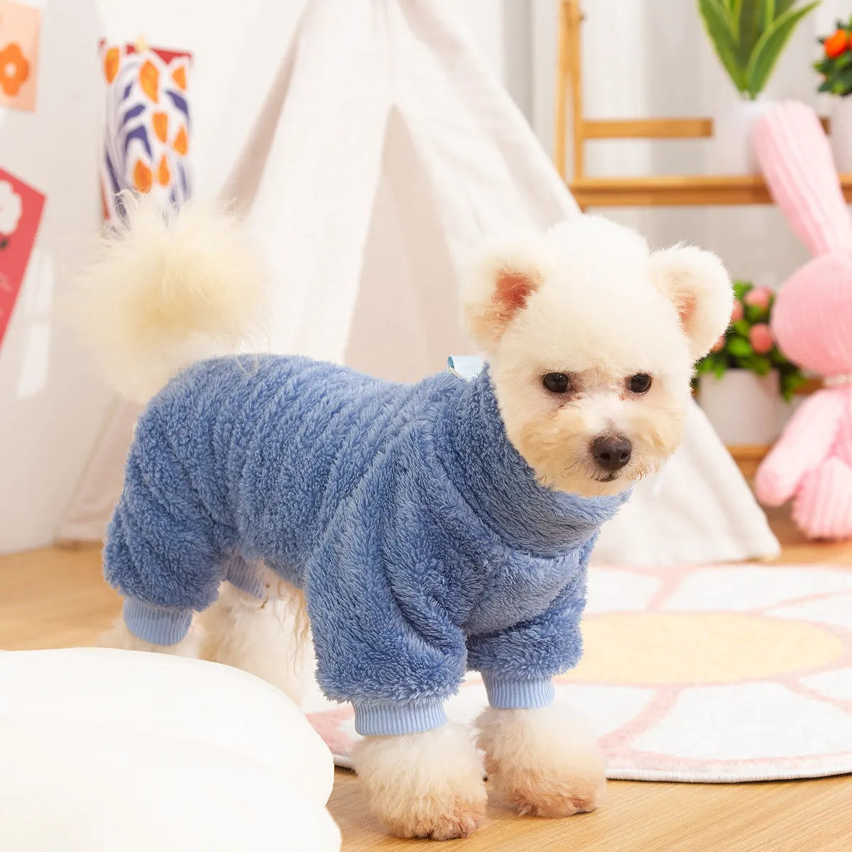 A dog wearing a blue four-legged plush jacket with a high collar and a tow ring on the back.