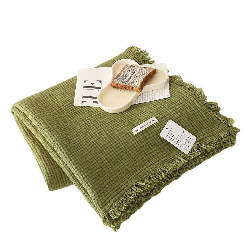 Four-layer gauze cotton blanket with tassel trim in avocado green colour draped over a sofa