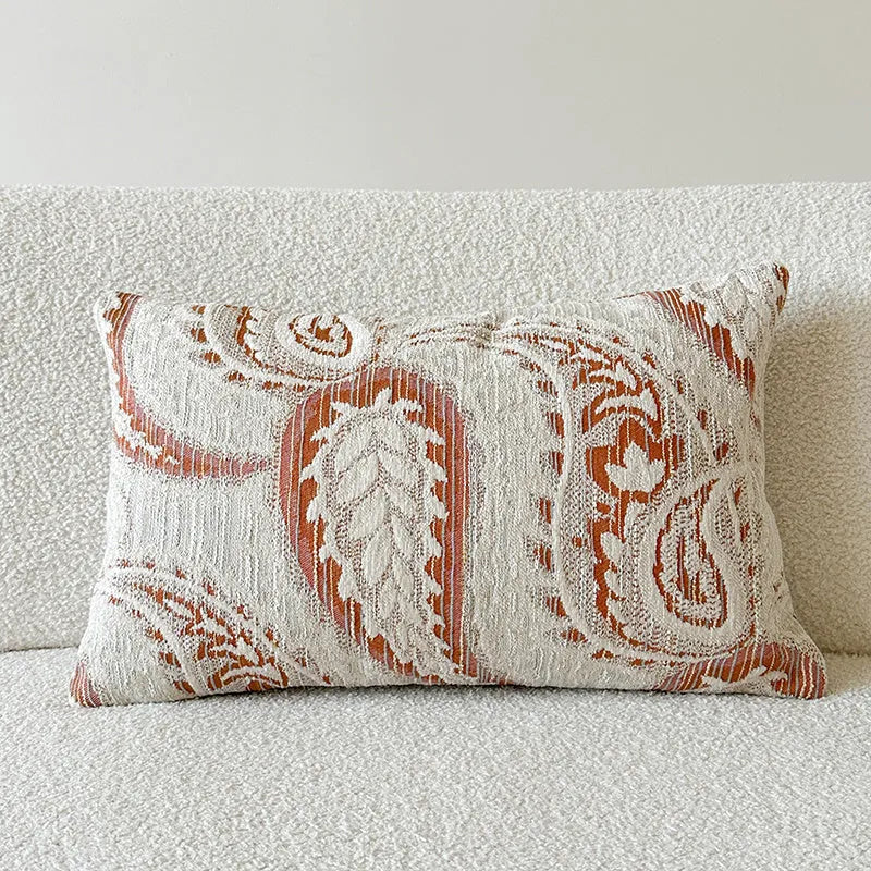 Amber-coloured jacquard pillow cover with paisley and flower pattern, shown in 45x45cm size on a sofa.