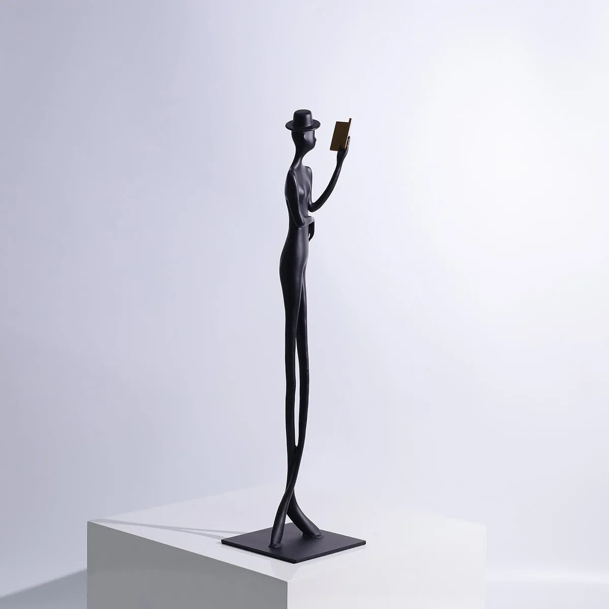Black cast aluminium reading woman sculpture on desktop, 12 cm wide by 51 cm high