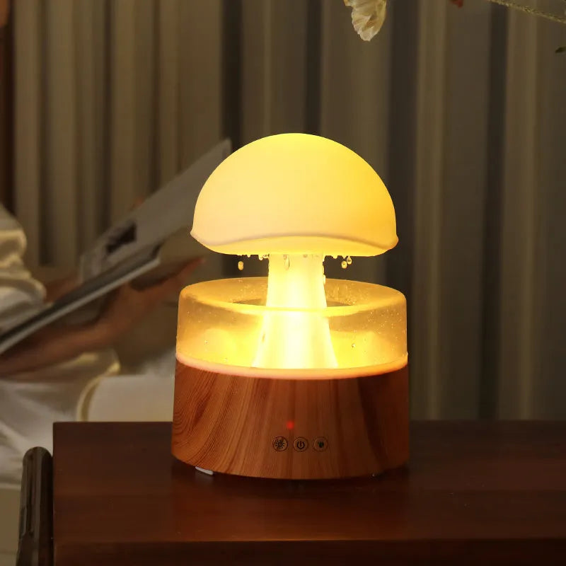 White cloud-shaped humidifier and aroma diffuser with LED lights and mist output on a wooden table.