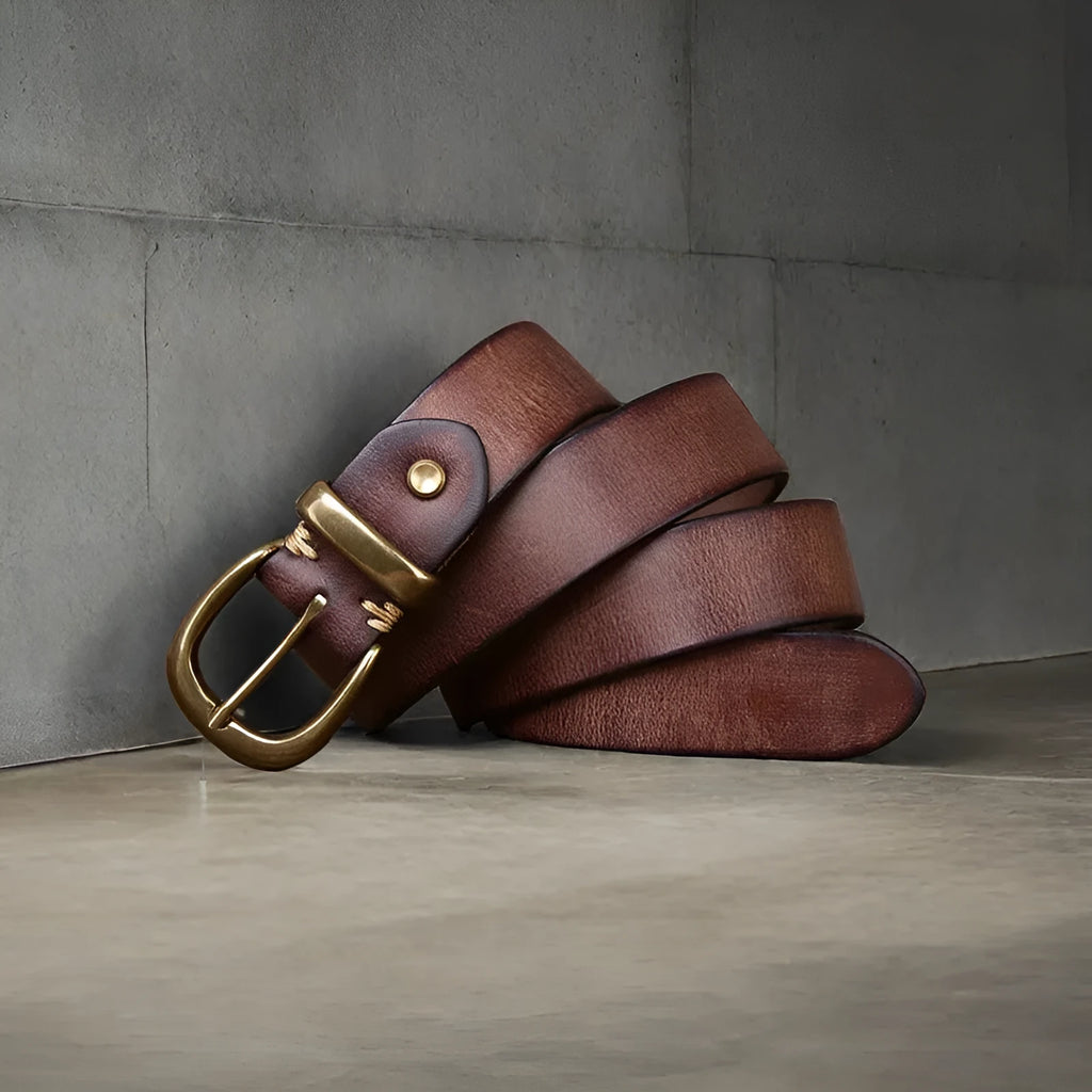 Men's black genuine cowhide leather belt with copper pin buckle on a jeans background.