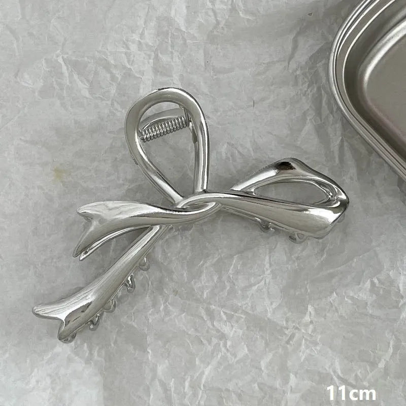 Assortment of silver metal hair claw barrettes with various designs including bows, pearls, and geometric shapes.