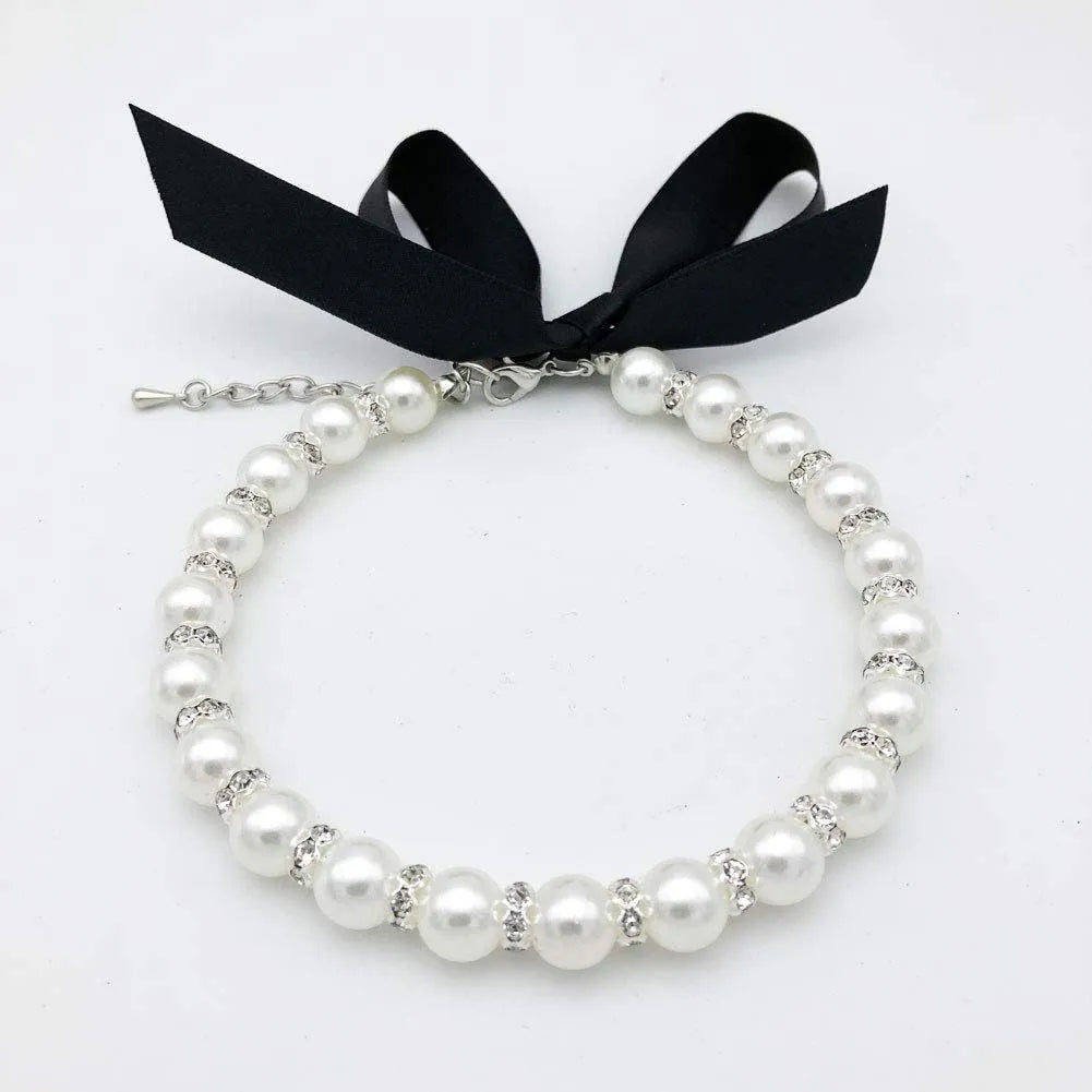 Small dog wearing blue imitation pearl and rhinestone necklace with adjustable clasp and ribbon bow