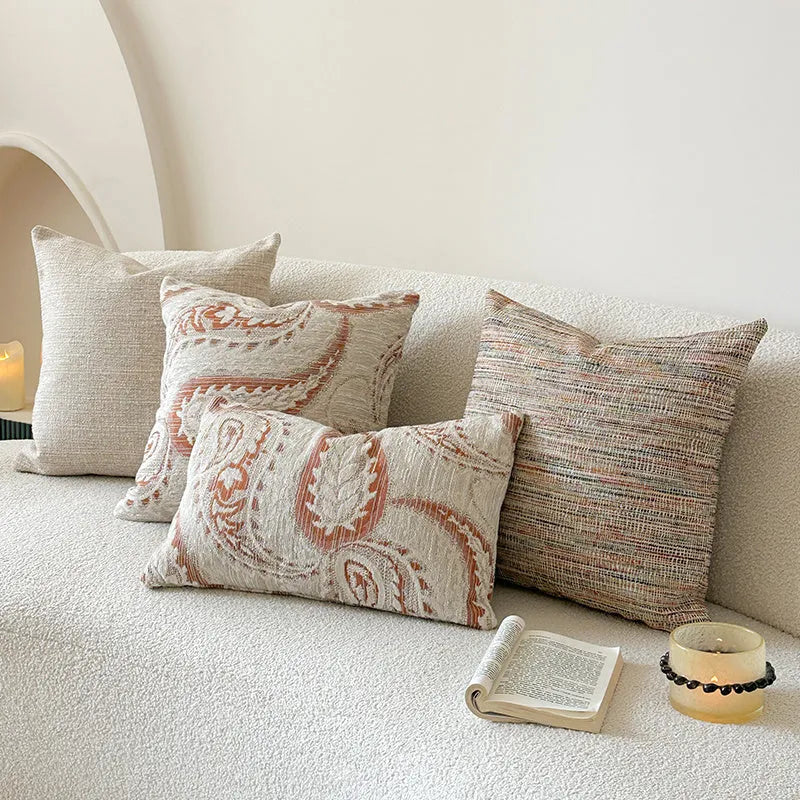 Amber-coloured jacquard pillow cover with paisley and flower pattern, shown in 45x45cm size on a sofa.