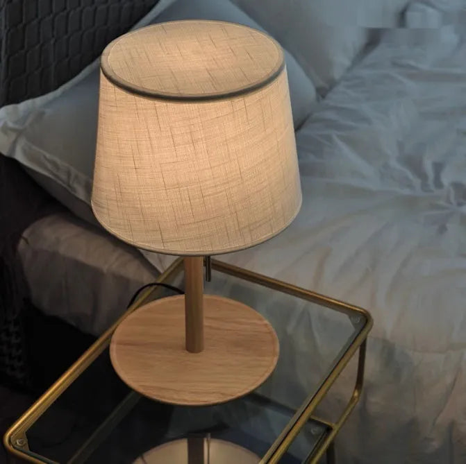Walnut-colour solid wood desk lamp with a white fabric shade on a wooden table.