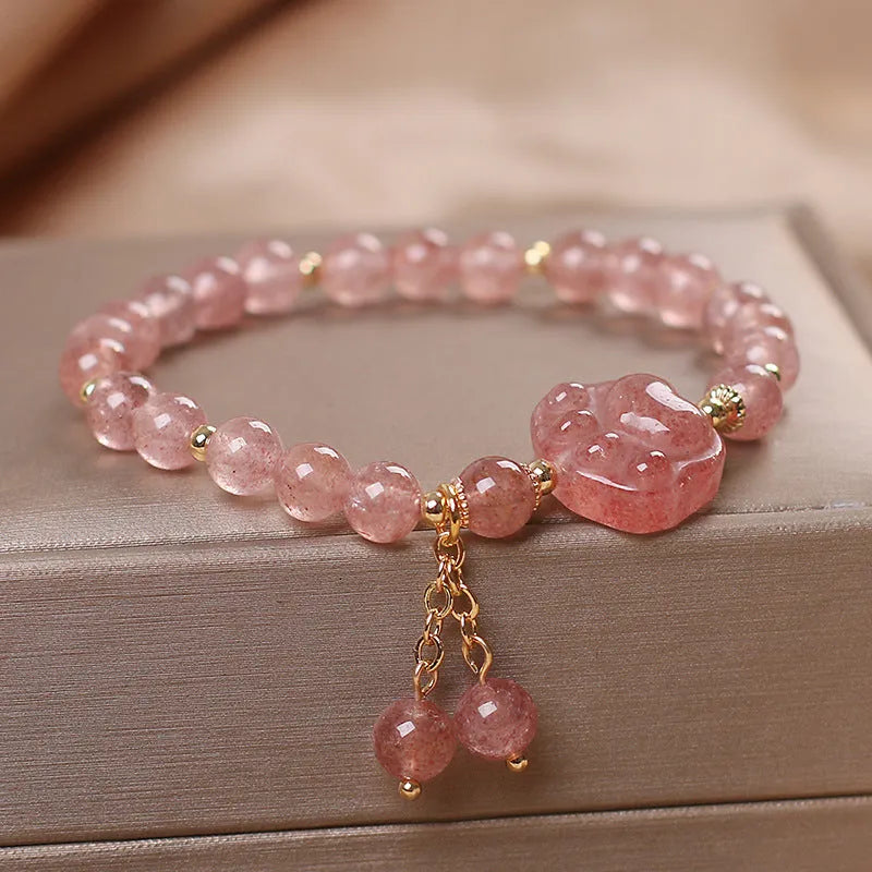 Women's double-layer strawberry quartz crystal bracelet with a red lucky cat charm on a white background.