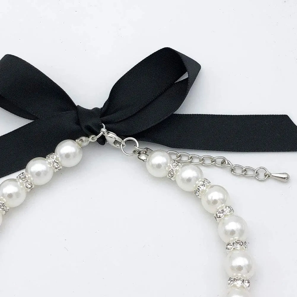 Small dog wearing blue imitation pearl and rhinestone necklace with adjustable clasp and ribbon bow