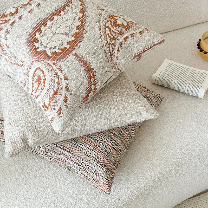 Amber-coloured jacquard pillow cover with paisley and flower pattern, shown in 45x45cm size on a sofa.