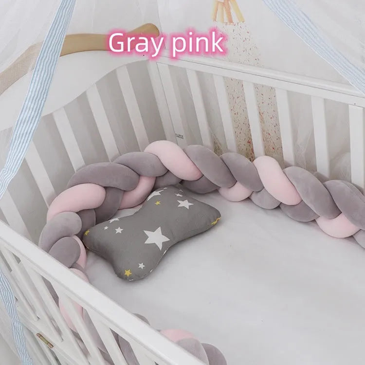 Braided knot style baby crib bumper in a light grey colour, shown lined inside a white wooden cot.