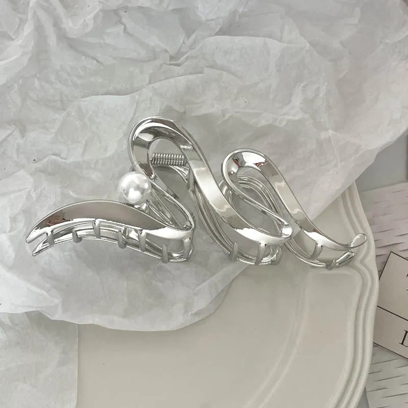 Assortment of silver metal hair claw barrettes with various designs including bows, pearls, and geometric shapes.