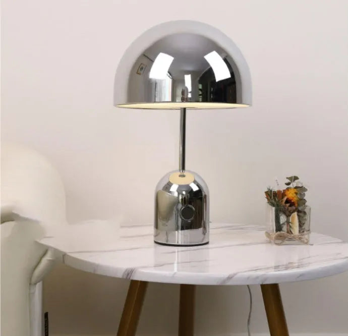 Mushroom-shaped table lamp with a metal base in rose gold finish on a wooden surface.