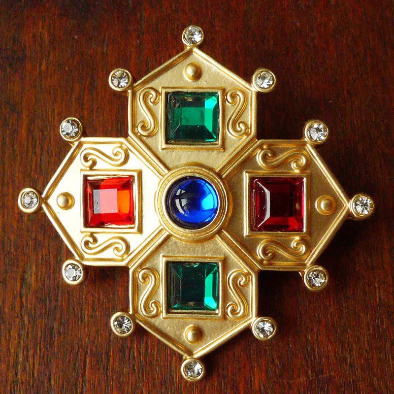 Close-up of a vintage baroque style zinc alloy brooch with a diamond shape on a dark fabric background.