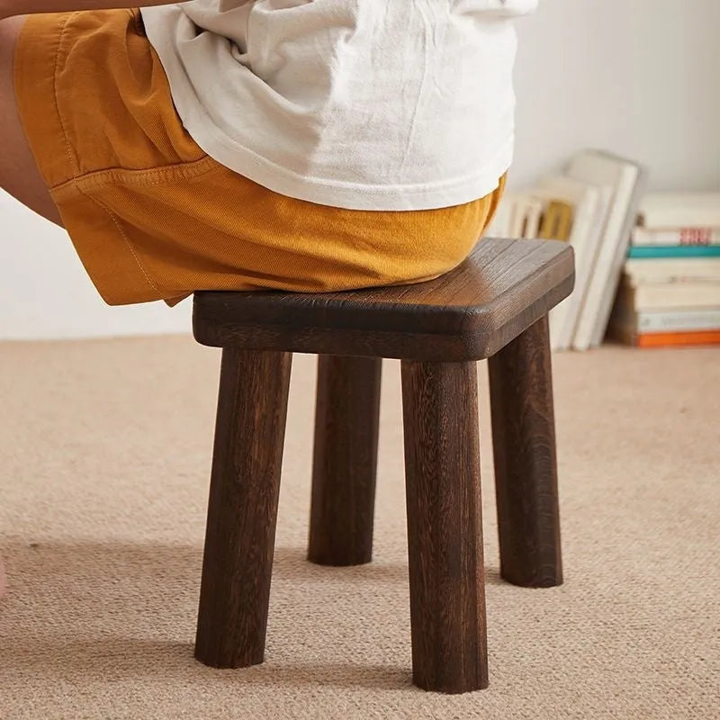 Distressed solid wood shoe changing stool with bracket structure, shown in a hallway setting.