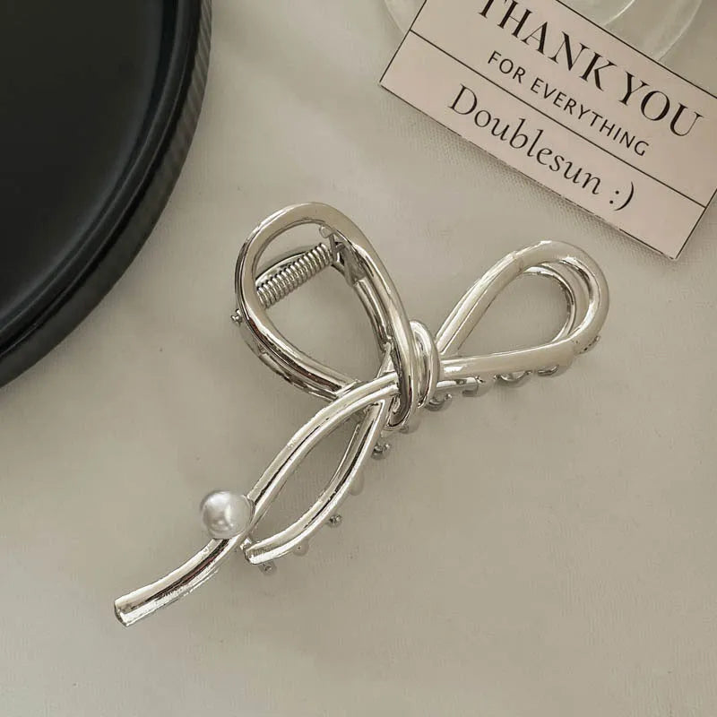 Assortment of silver metal hair claw barrettes with various designs including bows, pearls, and geometric shapes.